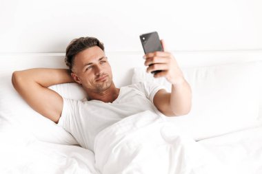 Yakışıklı adam yatakta döşeme sırasında cep telefonu tutan