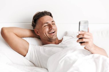 Yatakta döşeme sırasında cep telefonu kullanan adam gülüyor