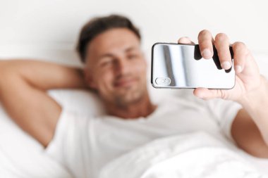 Gülümseyen adam yatakta döşeme sırasında cep telefonu ile bir selfie alarak yakın çekim