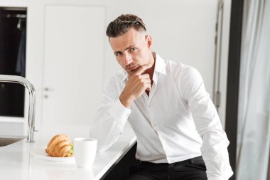 Adam büyüleyici bir mutfak üzerinde otururken kahvaltı resmi elbise giymiş.