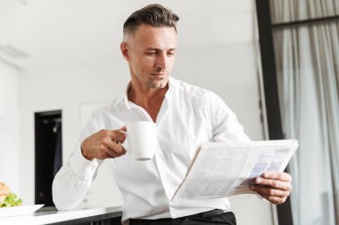 Resmi elbise kahvaltı bir mutfak ile bir gazete üzerinde otururken kendine güvenen adam giymiş