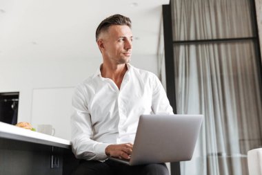 Başarılı adam evde oturan ve kahvaltı ederken dizüstü kullanarak resmi elbise giymiş