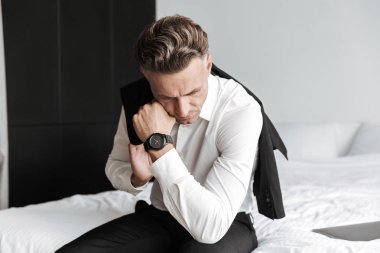 Yorgun adam yatakta oturuyor ve aşağı bakıyor takım elbise giymiş