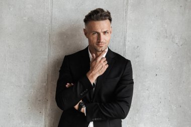 Başarılı adam kameraya gri duvar arka plan üzerinde seyir takım elbise giymiş