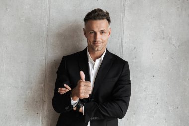 Yakışıklı adam jest Yaşasın gri duvar arka plan üzerinde gösterilen takım elbise giymiş