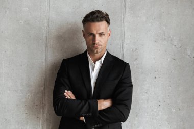 Kendine güvenen adam katlanmış ve kameraya gri duvar arka plan üzerinde seyir silah tutan takım elbise giymiş