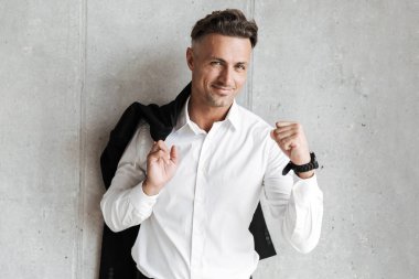 Yumruğunu gri duvar arka plan üzerinde gösterilen omzunun üzerinden ceket ile yakışıklı adam