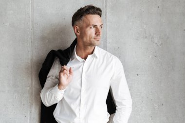 Yakışıklı adam uzakta gri duvar arka plan üzerinde seyir omzunun üzerinden ceket ile