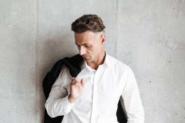 Çekici bir adam uzakta gri duvar arka plan üzerinde seyir omzunun üzerinden ceket ile