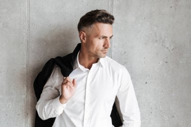 Uzak gri duvar arka plan üzerinde seyir omzunun üzerinden ceket ile kendine güvenen adam