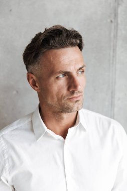 Beyaz gömlekli uzakta gri duvar arka plan üzerinde seyir yakışıklı bir adam portresi kapatın