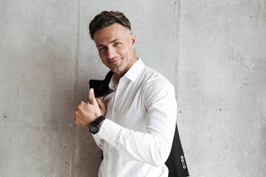 Jest Yaşasın gri duvar arka plan üzerinde gösterilen omzunun üzerinden ceket ile yakışıklı adam