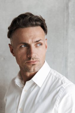 Uzak seyir gri duvar arka plan üzerinde beyaz gömlekli konsantre bir adam portresi kapatın