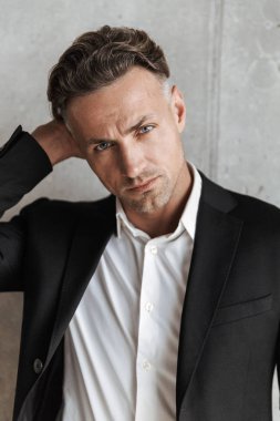 Kameraya gri duvar arka plan üzerinde seyir takım elbise giymiş çekici bir adam portresi kapatın