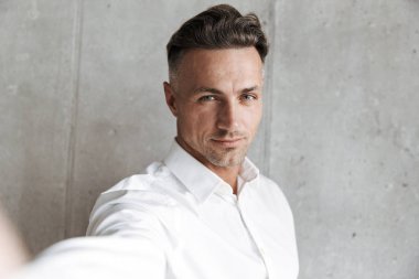 Beyaz gömlekli bir selfie ile outsretched alarak yakışıklı bir adam portresi el Gri duvar arka plan üzerinde