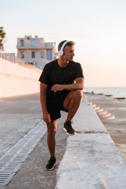 Plajda germe egzersizleri yapıyor kulaklık ile kendine güvenen bir sporcu tam uzunlukta