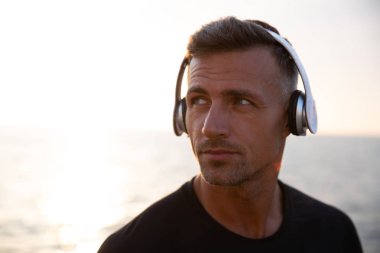 Fotoğraf portre yakışıklı Avrupa adamın 30'lu açıklarında açık yürüyüş sırasında kablosuz kulaklık ile müzik dinlemek t-shirt