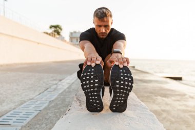 Isınma ve bacaklar Sahil yakınındaki gündoğumu sırasında germe eşofman konsantre güçlü adam 30'lu fotoğrafı