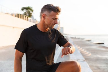 Eşofman yürüme Avrupa kaslı adam 30s boyunca tahta gündoğumu ve akıllı kol saati seyir sırasında Sahil yakınındaki fotoğrafı