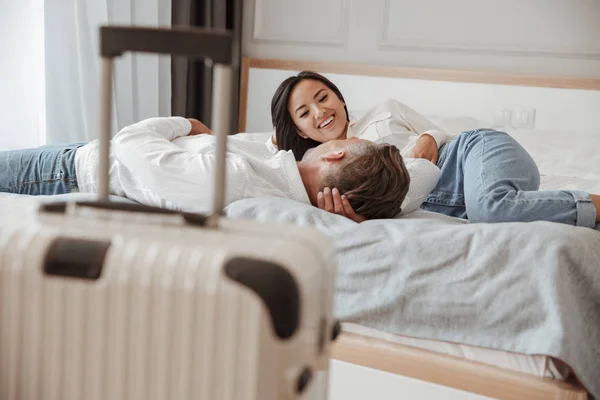 照片的幸福夫妇男女在休闲服装一起休息 躺在床上的酒店房间与行李附近的床 假期或度假概念 — 图库照片
