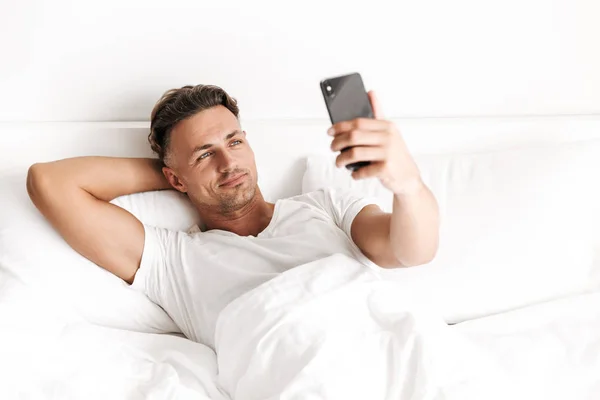 Hombre Guapo Sosteniendo Teléfono Móvil Mientras Está Acostado Cama —  Fotos de Stock