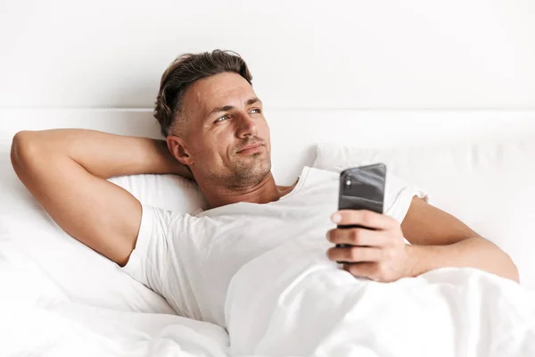 Pensivo Homem Segurando Telefone Celular Enquanto Deitado Cama — Fotografia de Stock