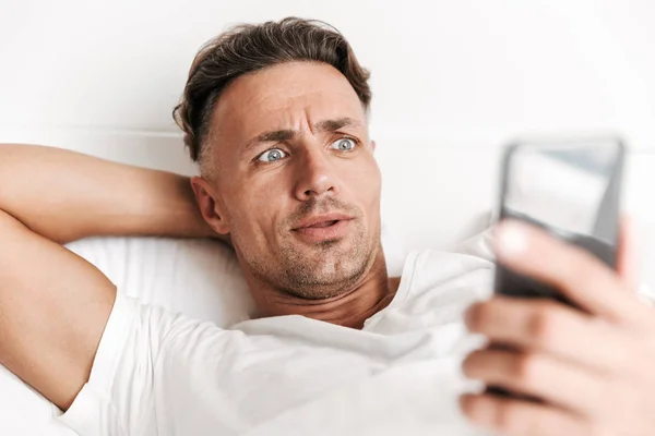 Zszokowany Człowieka Pomocą Telefonu Komórkowego Relaksując Się Łóżku Bliska — Zdjęcie stockowe