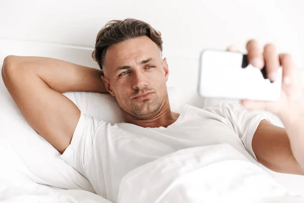 Yakışıklı Adam Yatakta Döşeme Sırasında Cep Telefonu Ile Bir Selfie — Stok fotoğraf