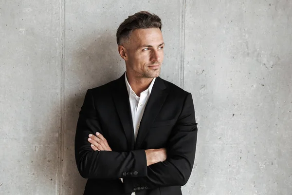 Handsome man dressed in suit holding arms folded and looking away over gray wall background