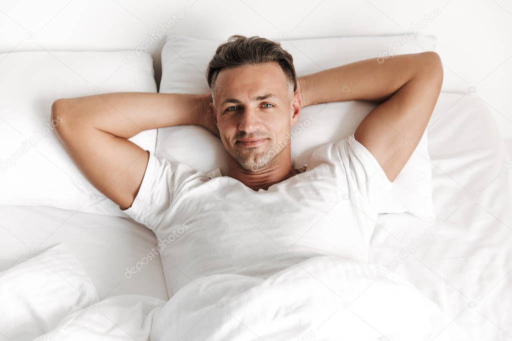 Smiling man relaxing in bed and looking at camera