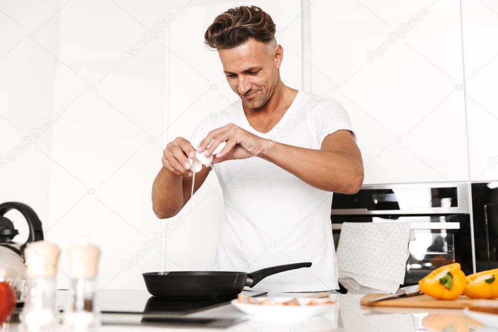 Happy man cooking eggs for breakfast while standing at a kitchen