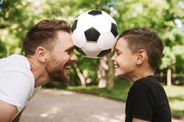 Resmi mutlu genç baba var eğlenceli küçük oğlu ile açık havada futbol topu ile park doğada.