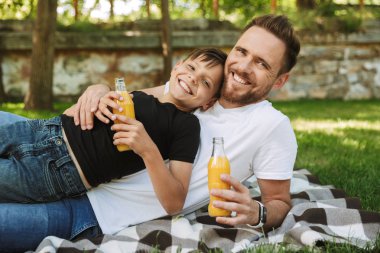Mutlu genç baba oğlunun açık havada park doğada suyu içme ile oturan görüntüsü. Görünümlü kamera.