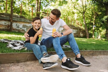 Mutlu genç baba oğlunun açık havada park doğada suyu içme ile oturan görüntüsünü.