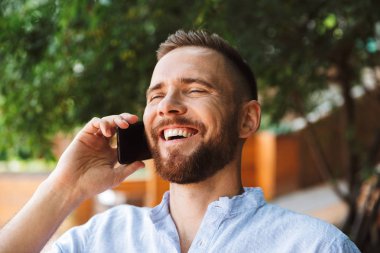 Mutlu sakallı yakışıklı genç bir kenara cep telefonuyla konuşurken açık havada bakış fotoğraf.
