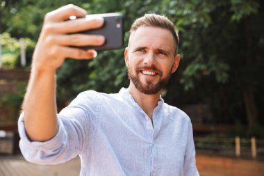 Açık havada cep telefonuyla bir selfie almak neşeli duygusal Genç sakallı adam fotoğraf.