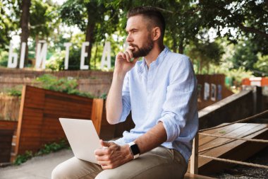 Konsantre Genç sakallı adam açık havada dizüstü bilgisayar kullanan resmi.