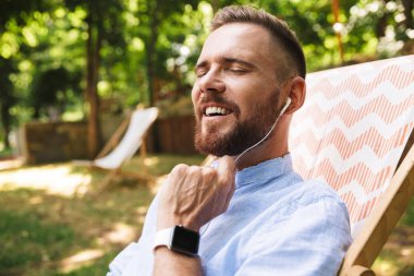Mutlu genç sakallı adam açık havada dinleme müzik kulaklık ile fotoğraf.