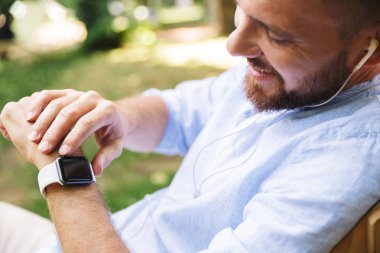 Mutlu genç sakallı adam açık havada dinleme müzik izle kullanarak kulaklık ile fotoğraf.