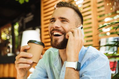 Mutlu sakallı yakışıklı genç bir kenara cep telefonuyla konuşurken açık havada bakış fotoğraf.