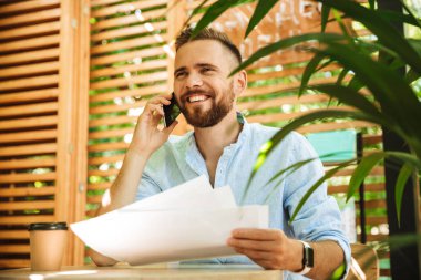 Açık havada belgeleri tutan cep telefonuyla konuşan Genç sakallı adam görüntüsünü.