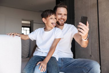 Neşeli genç adam baba baba oğluyla evde kapalı cep telefonuyla görüntü.