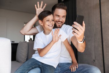 Mutlu genç adam baba baba oğluyla kapalı ev sallayarak, cep telefonuyla fotoğrafını.