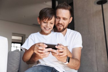 Yakışıklı sakallı adam kapalı evde onun oğlu çocuk ile görüntü oyun oyunlar cep telefonu tarafından.
