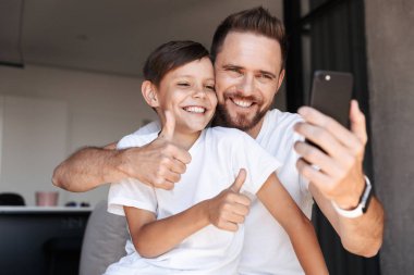 Cep telefonu kullaranarak onun oğlu çocuğuna yapmak bir selfie almak Yaşasın jest imge-in yakışıklı sakallı adam kapalı evde.