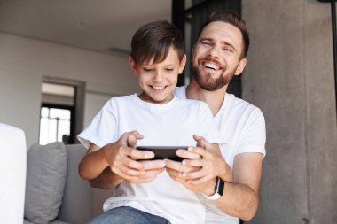 Yakışıklı sakallı adam kapalı evde onun oğlu çocuk ile görüntü oyun oyunlar cep telefonu tarafından.
