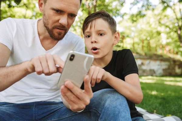 Döbbenve Fiatal Apa Ült Kis Fia Szabadban Mobiltelefon Használata Park — Stock Fotó