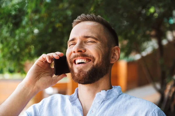 Mutlu sakallı yakışıklı genç bir kenara cep telefonuyla konuşurken açık havada bakış fotoğraf.