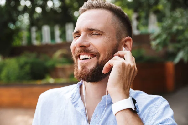 Mutlu genç sakallı adam açık havada dinleme müzik kulaklık ile fotoğraf.