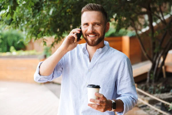 Mutlu genç sakallı adam açık havada kahve içme cep telefonuyla konuşurken fotoğrafı.